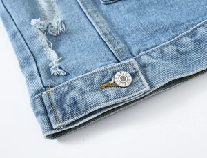 Detail van lichtblauw spijkerjasje met gerafelde randen en zilveren metalen JEANS knoop