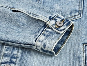 Close-up of light blue denim jacket cuff with metal JEANS button and yellow stitching
