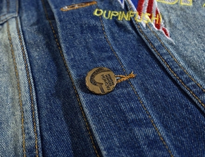 Detailed close-up of dark blue denim vest featuring vintage metal button and yellow embroidery