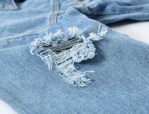 Detailopname van lichtblauw spijkerjack met distressed details en gerafelde randen