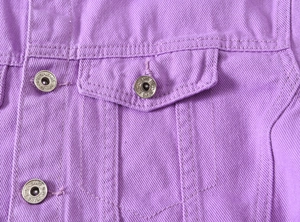 Detail of purple denim jacket featuring a metal button and reinforced flap pocket