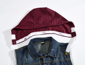 Détail d'un gilet en denim bleu avec capuche bordeaux amovible et fixation par boutons