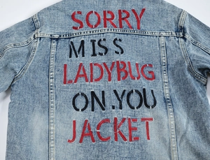 Men's light blue washed denim jacket featuring bold red letter embroidery on the back