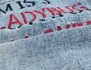 Detail of light blue washed denim jacket with high-quality MISS LADYBUG letter embroidery