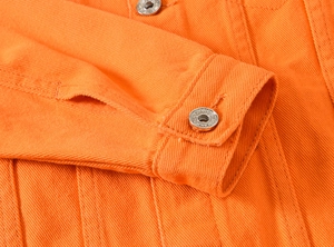 Detail einer hellorangen Jeansjacke mit gravierten Silbermetallknöpfen und Webstruktur