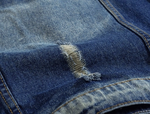 Detailed close-up of blue denim vest fabric with distressed holes and stone-washed effect
