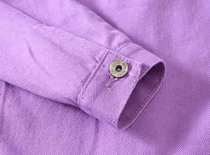 Close-up of purple denim jacket cuff with silver metal button featuring NEW JEANS text