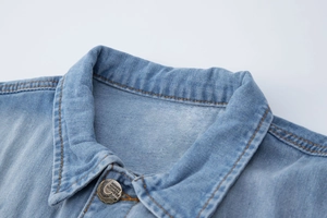 Détail du col d'un gilet en jean bleu clair avec coutures oranges et bouton vintage