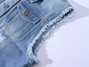 Détail du bord effiloché de la manche et bouton métallique vintage sur gilet denim bleu