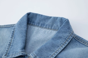Détail du gilet en jean bleu clair montrant le revers classique et les surpiqûres jaunes