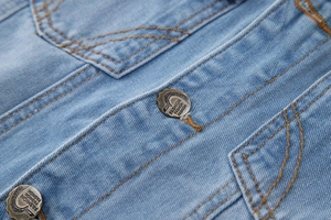 Détail macro du gilet en denim pour homme avec surpiqûres orange et bouton en métal gravé