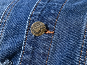 Macro shot of denim jacket detail with copper button and orange topstitching