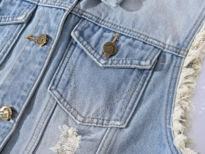 Detail of light blue denim vest showing fringe edges and heart-shaped metal buttons