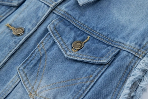 Détail du gilet en jean bleu délavé avec boutons en métal et bords effilochés