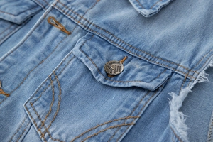 Détail macro d'une poche de gilet en jean bleu clair avec bouton métal et bords effilochés
