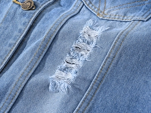 Détail macro d'un gilet en jean pour homme avec lavage clair et bouton coeur en bronze