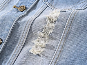 Macro shot of light blue denim vest showing distressed holes and heart-shaped metal button