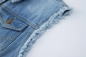 Détail du gilet en jean bleu clair montrant l'ourlet effiloché et le bouton en métal