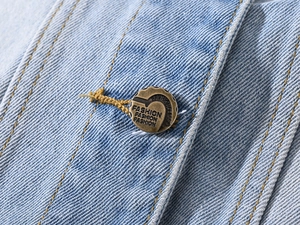 Macro shot of a bronze metal button with Fashion engraving on light blue denim vest