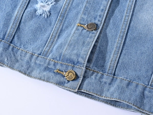 Détail du gilet en jean bleu clair montrant la texture sergée, l'usure et boutons en métal