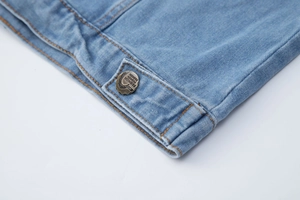 Détail macro de l'ourlet en denim bleu clair avec bouton vintage et coutures jaunes