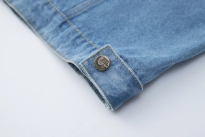 Détail d'un gilet en jean bleu clair avec bouton en bronze et surpiqûres jaunes contrastées