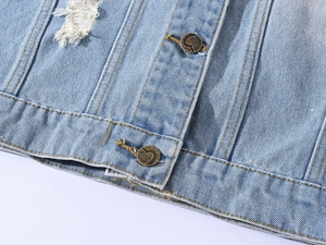 Detailed macro view of light blue denim fabric with distressed holes and vintage metal buttons