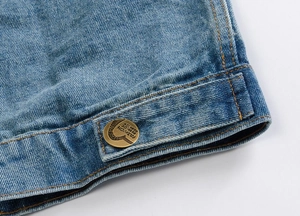 Detailed macro view of vintage brass button and orange stitching on blue denim vest