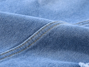 Gros plan sur le denim bleu clair avec des surpiqûres jaunes et des bords effilochés