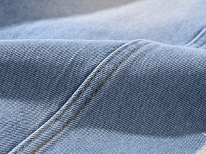Detailed close-up of light blue denim fabric with double yellow stitching and frayed edges