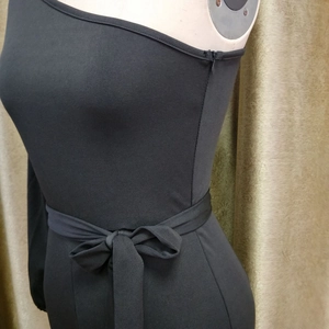 Detail of black one-shoulder jumpsuit featuring a waist tie and side zipper closure