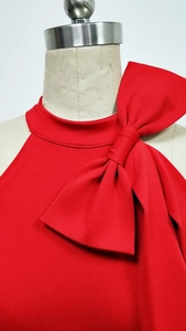 Detail eines roten Neckholder-Jumpsuits mit einer großen Schleife und feiner Stoffstruktur