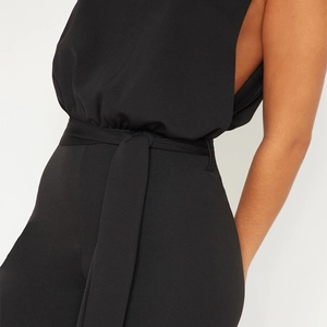 Detail view of black sleeveless jumpsuit showing the waist tie and smooth fabric texture