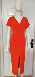Detail view of orange V-neck dress featuring elegant side ruching and a slit hemline
