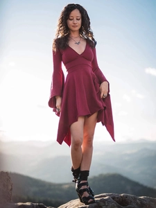 Detail of burgundy V-neck dress with flare sleeves and asymmetric hem against a mountain view