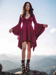 Deep V-neck wine red dress with dramatic bell sleeves and irregular hem in outdoor setting