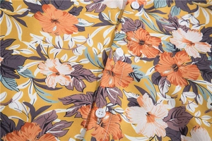 Detail of tropical hibiscus print on mustard yellow Hawaiian shirt with white buttons
