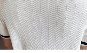 Close-up of white knitted polo shirt showing herringbone pattern and striped cuff