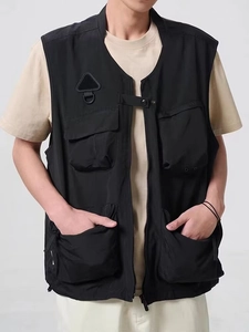 Detail view of black functional cargo vest featuring multiple utility pockets and D-ring