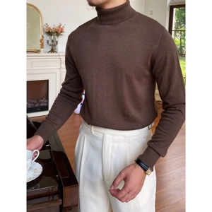 Schmal geschnittener, dunkelbrauner Rollkragenpullover für Herren mit weißer Hose im Raum