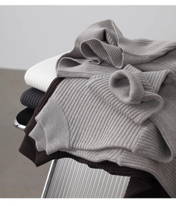 Detailed view of ribbed knit sweaters in various neutral colors stacked on a chair