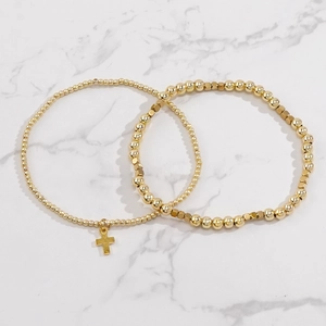 Detailed close-up of gold beaded bracelet set with cross pendant on marble background