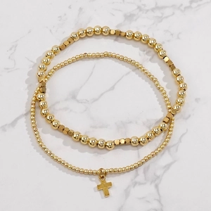 Layered gold beaded bracelets set with cross pendant on white marble background