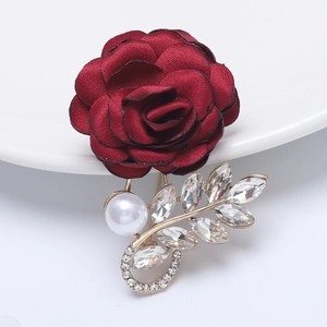Macro shot of a red fabric rose brooch with crystal leaves and a white pearl on a plate