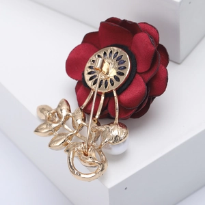 Elegant red fabric flower brooch with golden leaves and pearl detail on a white stand
