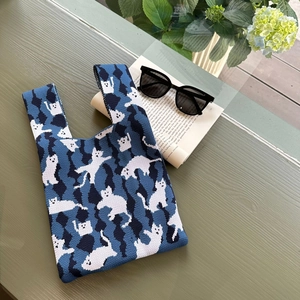 Detail of blue knitted tote bag with white cat patterns on a cozy wooden table set