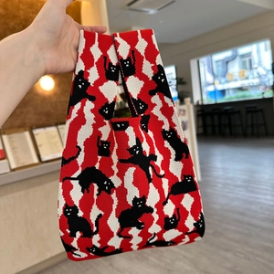 Close-up of knit tote bag featuring playful black cat patterns in red and white