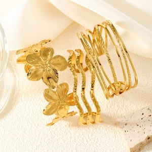 Detailed shot of three gold floral steel bracelets on elegant satin fabric background