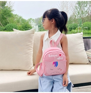 Pink cartoon unicorn canvas backpack worn by a little girl in an outdoor garden setting