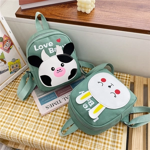 Close-up of green canvas mini backpacks with cute cartoon cow and rabbit embroidery
